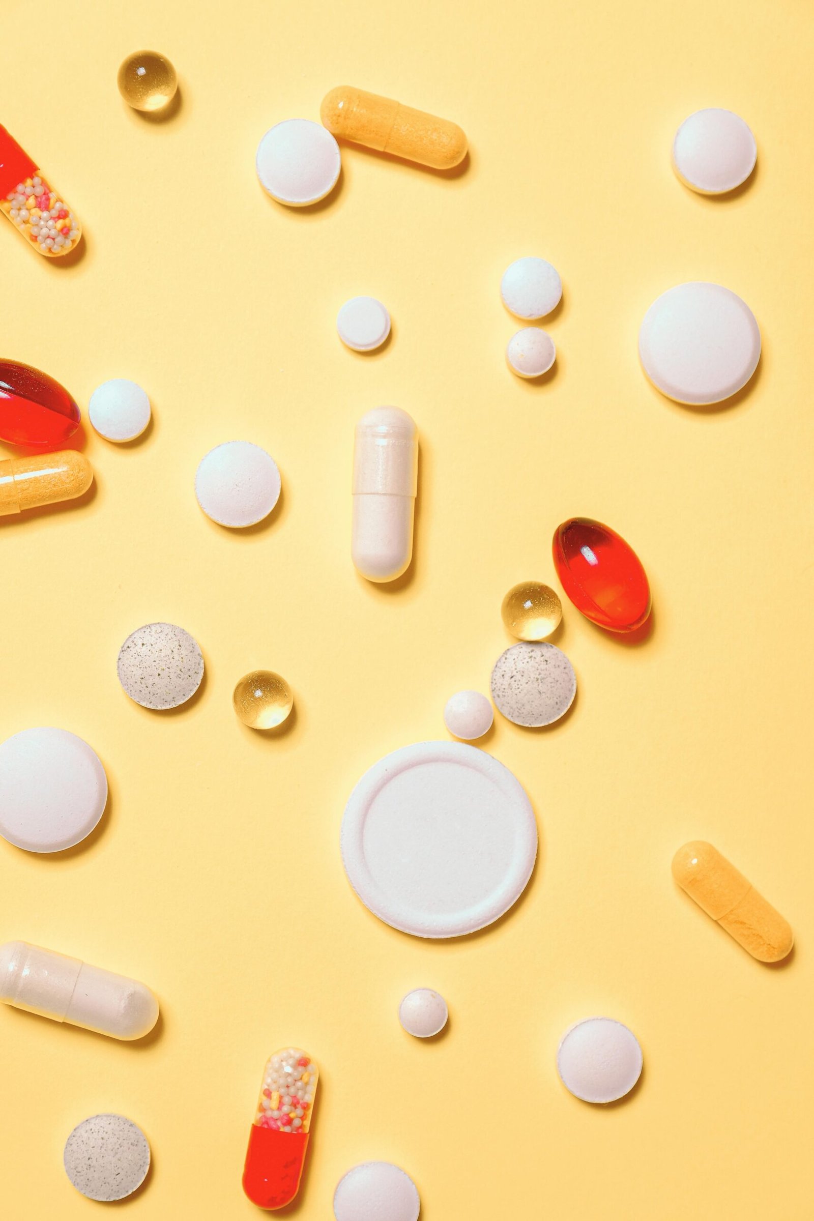 Colorful assortment of pills and capsules on a vibrant yellow background.